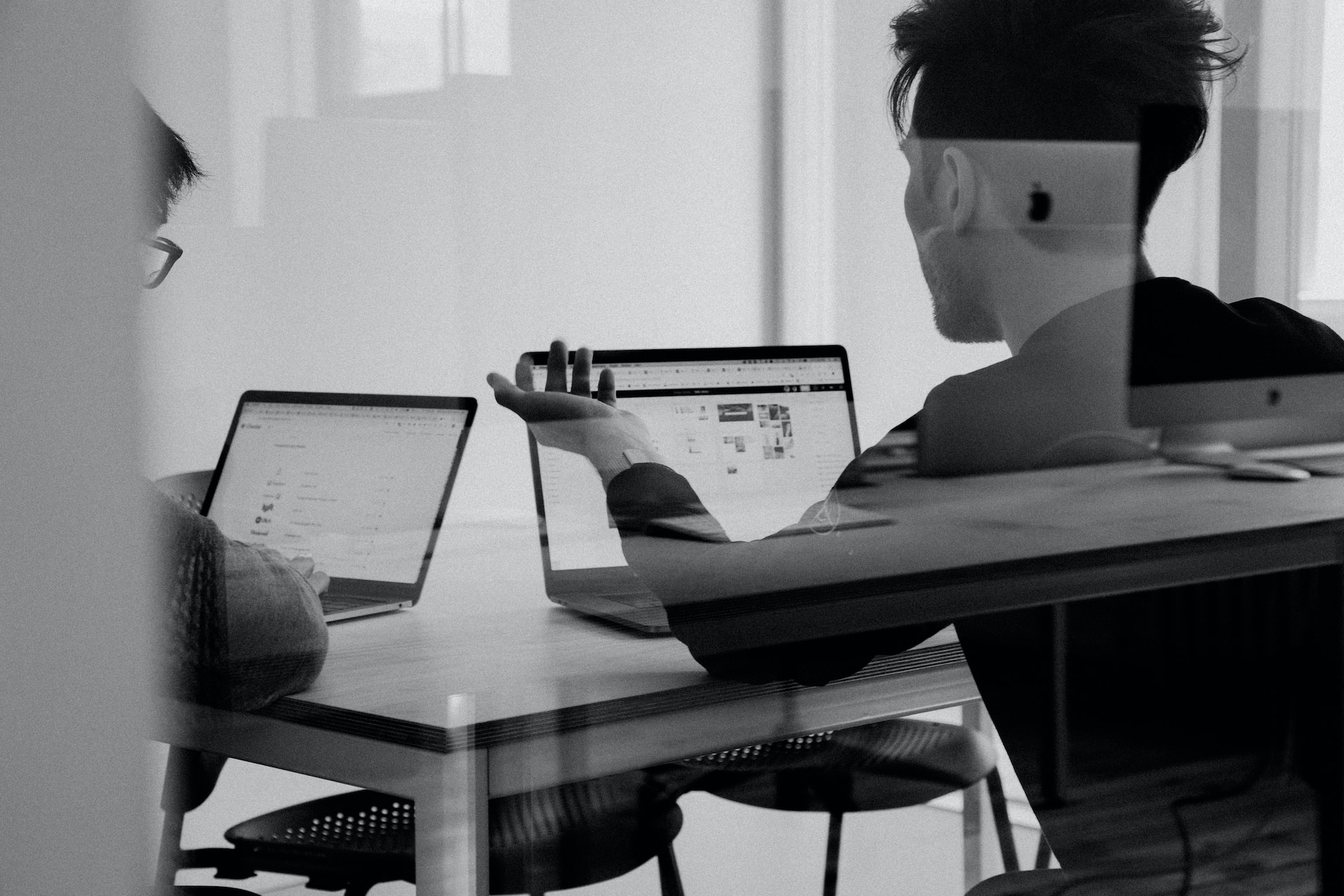 Schwarz-Weiß Bild zweier Personen von hinten, die auf ihre Laptops schauen und reden